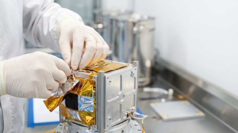 A technician assembles a small satellite technology component. Source:Adobe Stock (licensed).